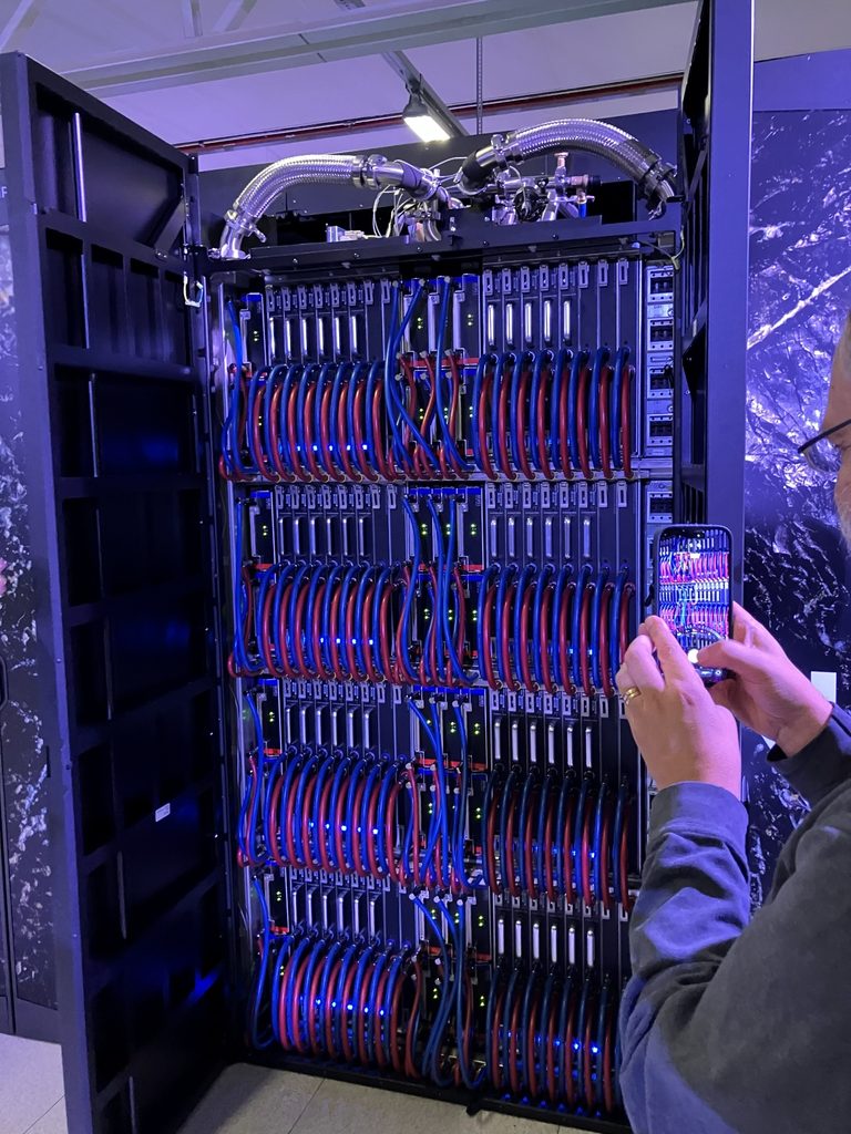 Närbild av superdatorn ARRHENIUS med röda och blå kylslangar. En besökare fotograferar utrustningen.